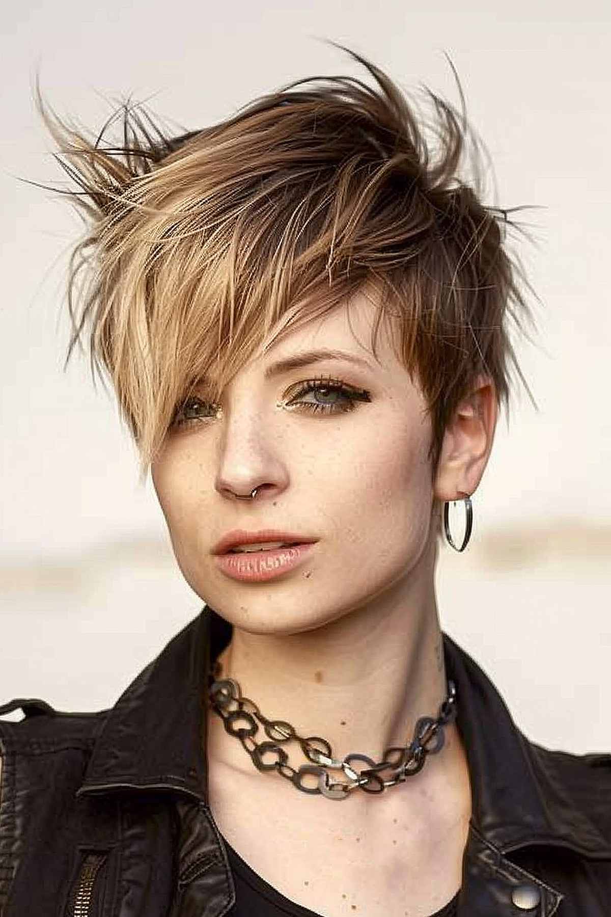 Edgy punk pixie cut with angular, asymmetrical bangs in multi-tonal blonde and brown, designed to add volume and emphasize facial features.