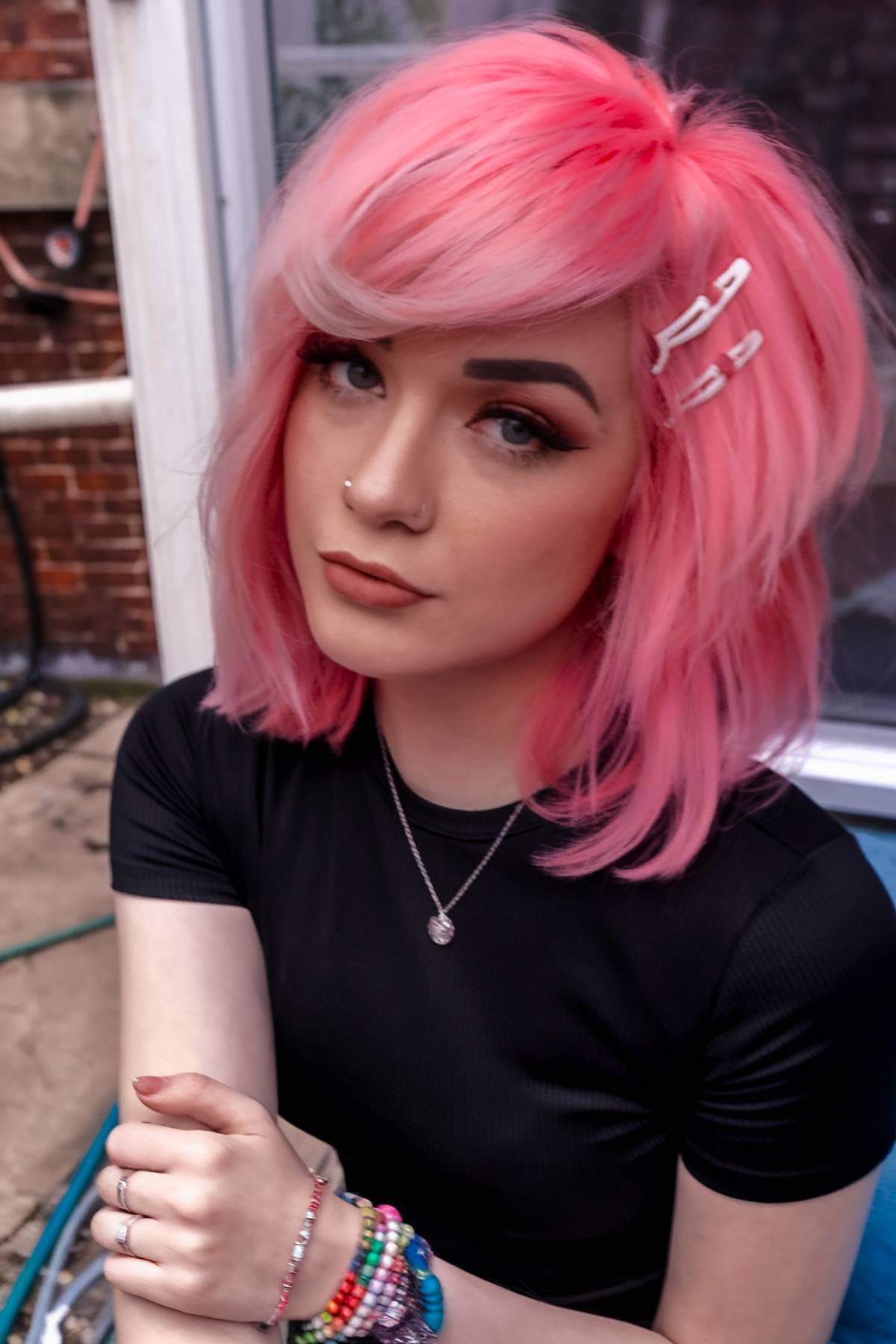 Pastel pink Y2K-inspired emo hairstyle with layered ends, voluminous side-swept bangs, and white hair clips