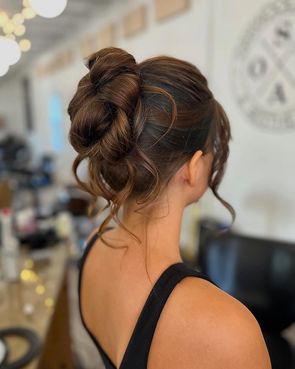 Sculpted twisted bun with romantic curls, perfect for homecoming hairstyles on medium to long thick brunette hair