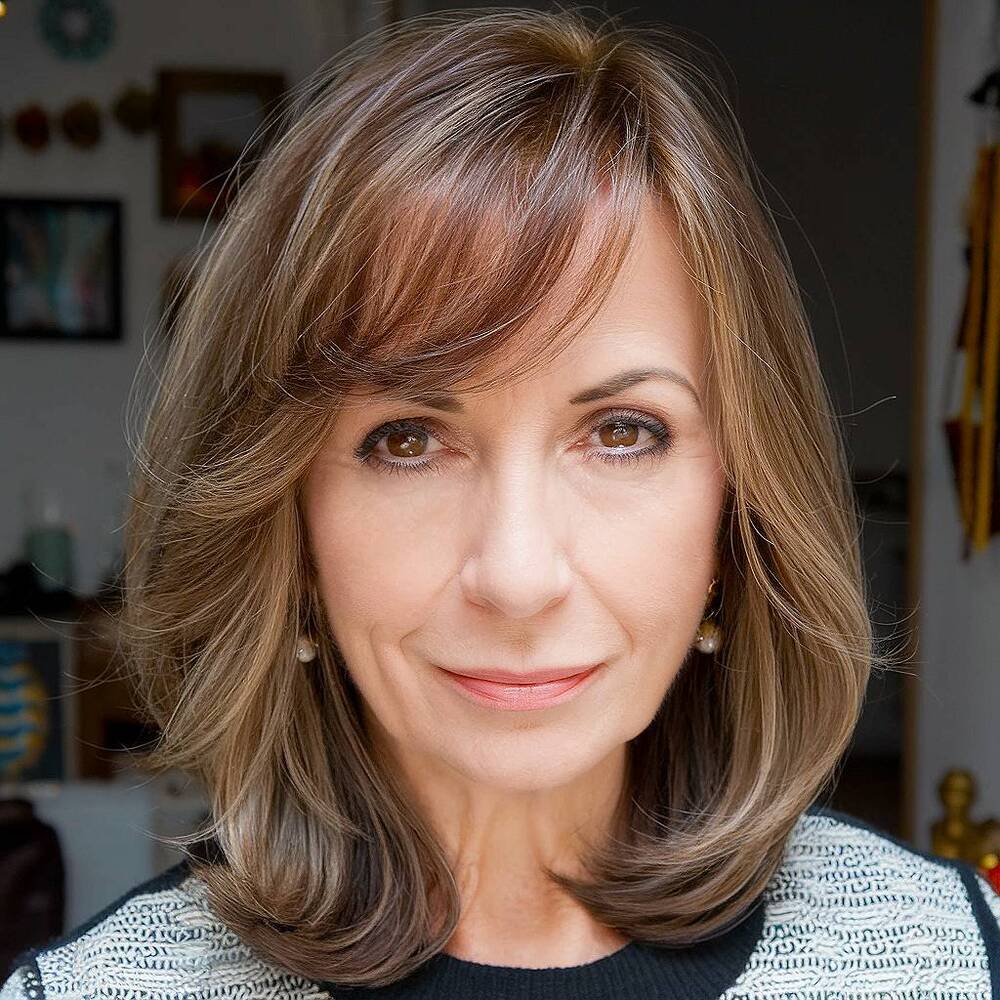 Medium-length layered haircut with side-swept bangs, perfect for adding softness and movement for women over 60