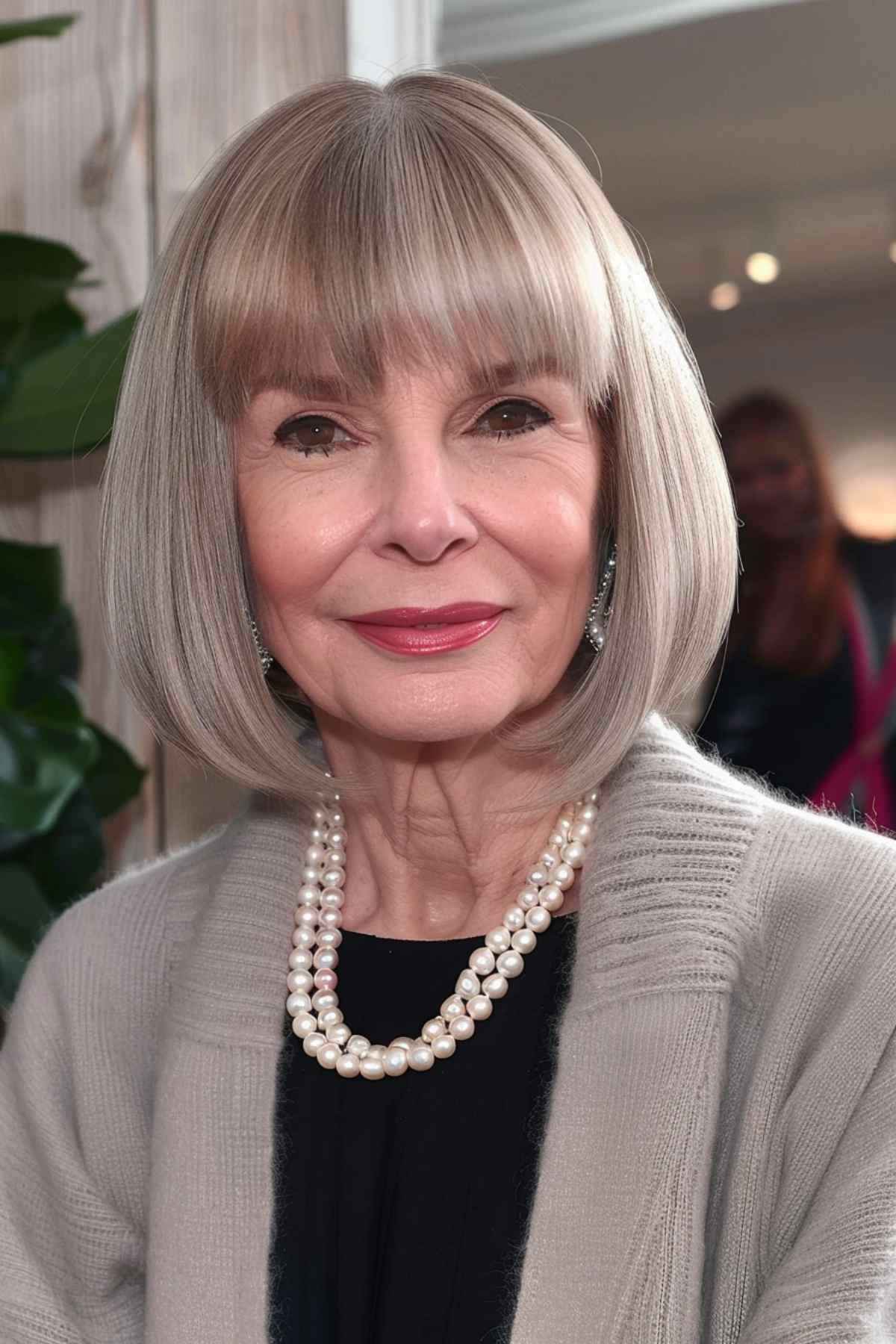 Mature woman with a sleek chin-length bob and straight bangs, adorned with a pearl necklace.