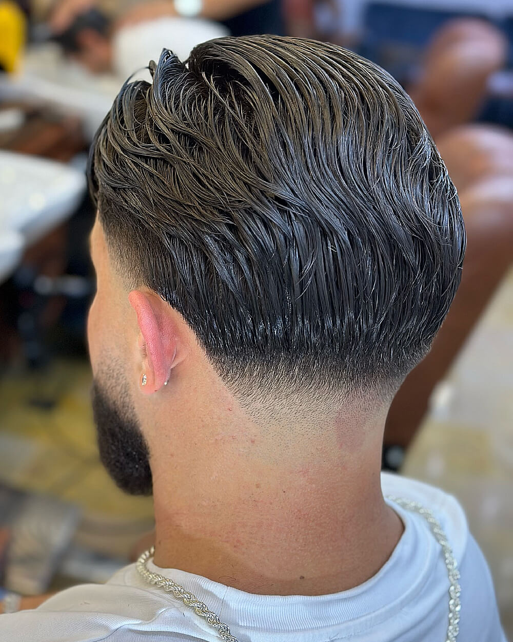 Slicked back layered hairstyle with a sharp low taper fade for men with dense hair