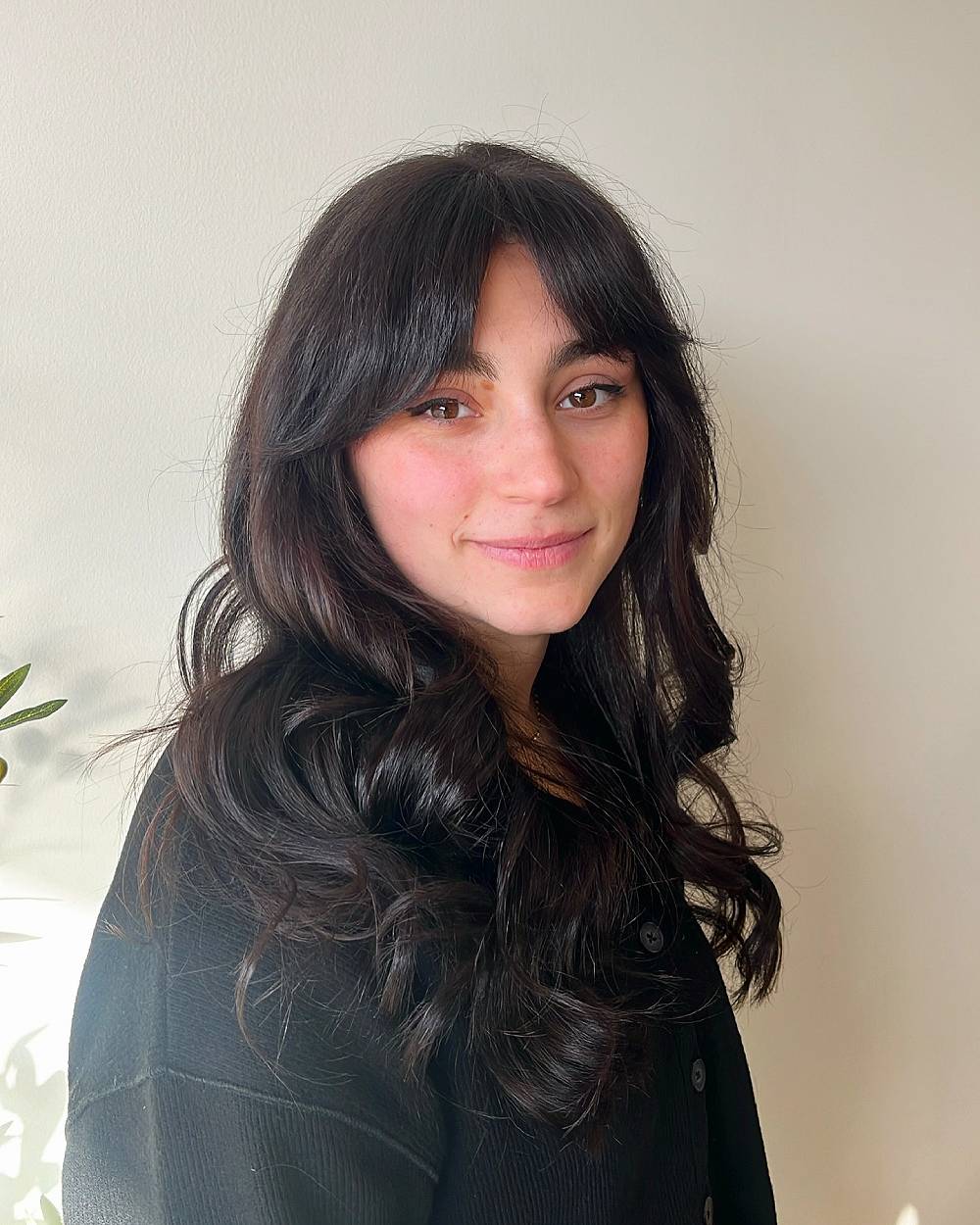 Soft layered waves with French bangs on long dark hair, adding volume and face-framing shape for a romantic, modern look