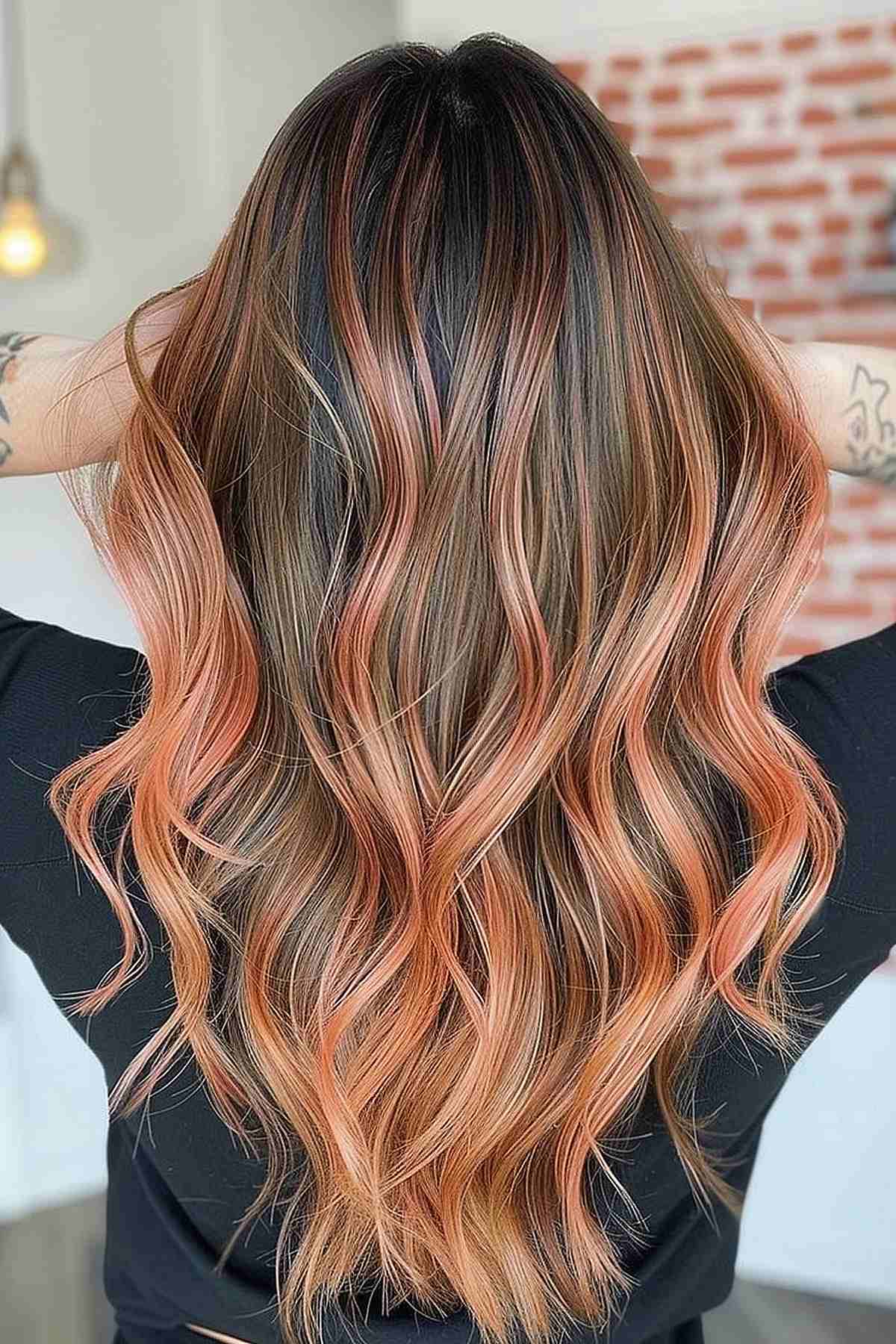 Long brunette hair with a soft peach balayage, featuring a color melt from dark roots to peach ends, enhanced by luxurious waves.