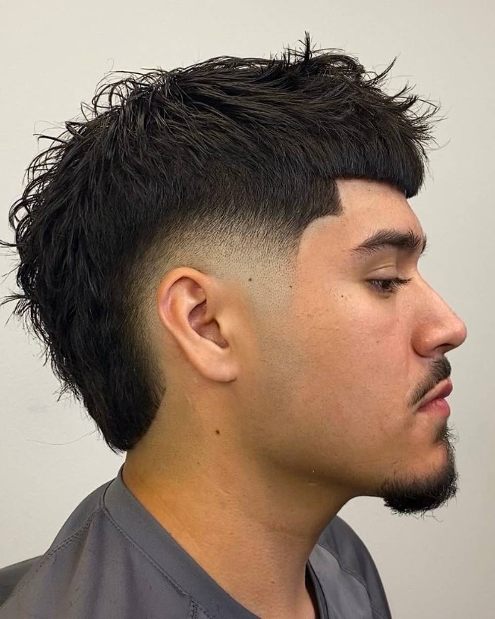 Textured mullet with burst fade and blunt fringe, styled for thick hair with edgy, modern contrast