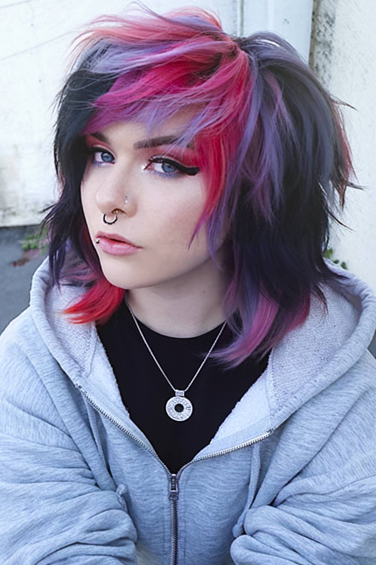 Layered 80s-inspired emo haircut with pink, purple, and black streaks and choppy bangs