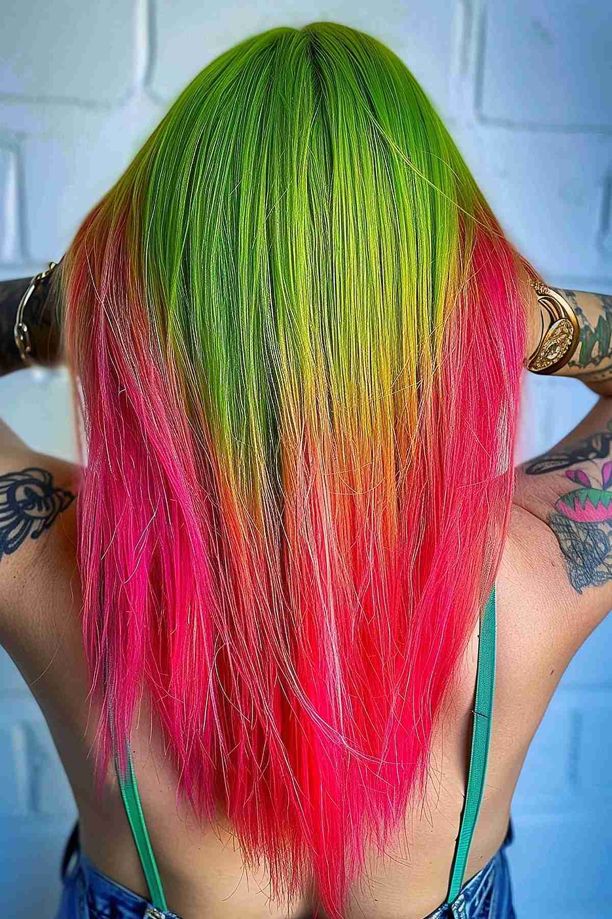 A woman's long, straight hair displaying a dramatic color transition from lime green at the roots through yellow to flamingo pink and red at the tips, embodying a fiery watermelon-inspired look.