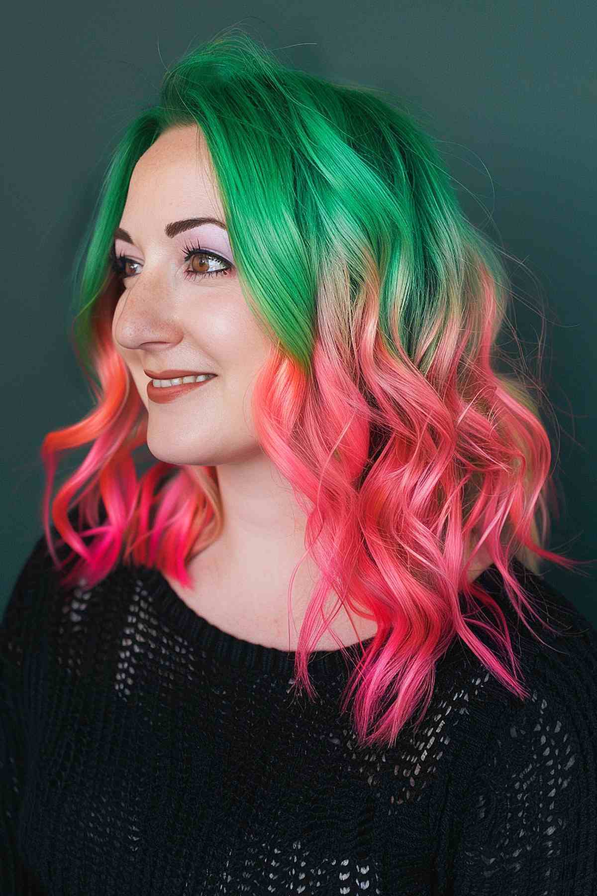 Wavy medium-length hair featuring a vibrant watermelon ombre, with green roots blending into pink ends, styled to showcase the bold color transition.