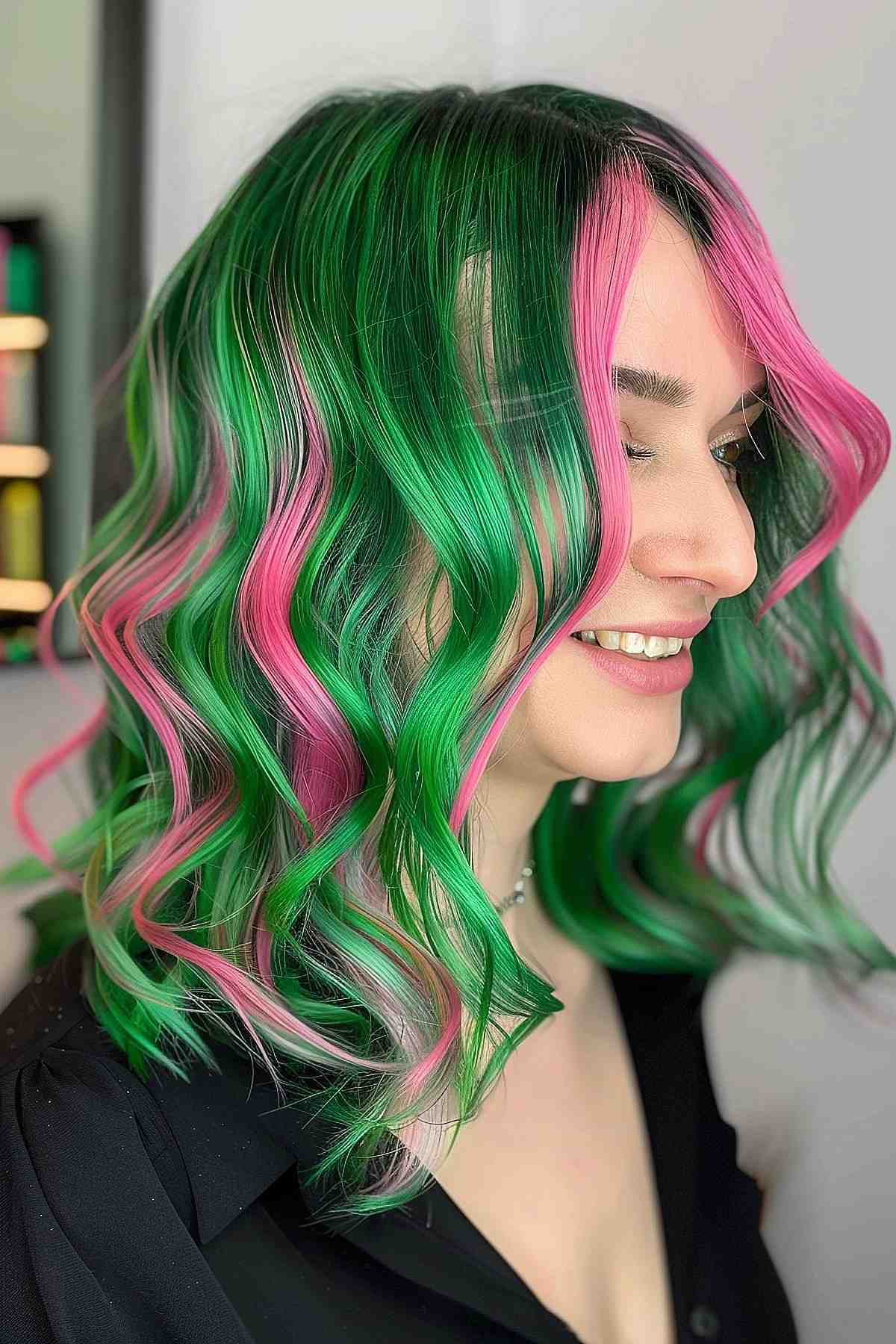 Medium-length wavy hair dyed in vibrant green and pink streaks, inspired by watermelon colors, styled to highlight bold color contrasts.