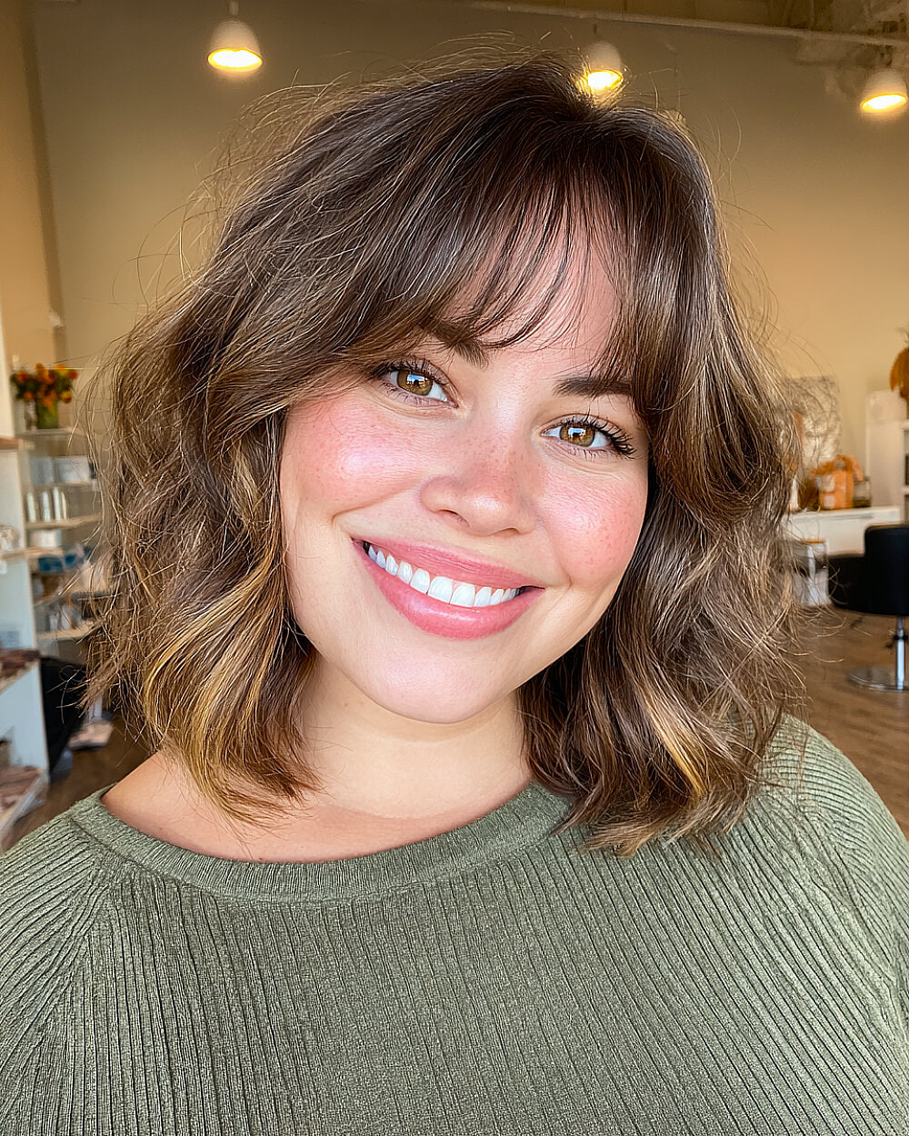 Wavy bob with wispy curtain bangs for round face, textured shoulder-length cut with soft layers and natural brunette highlights
