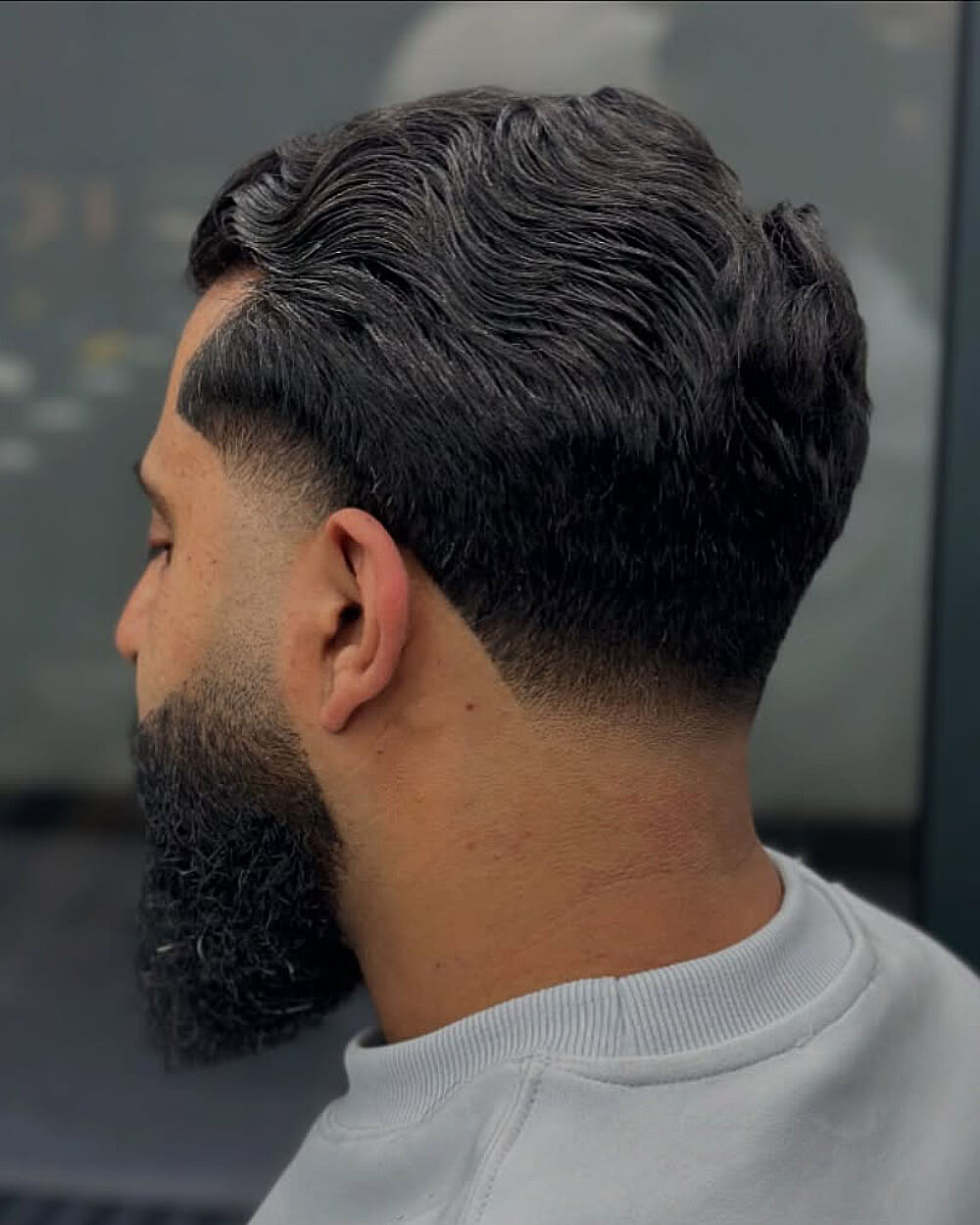 Men’s wavy side part haircut with a soft low taper fade for natural texture