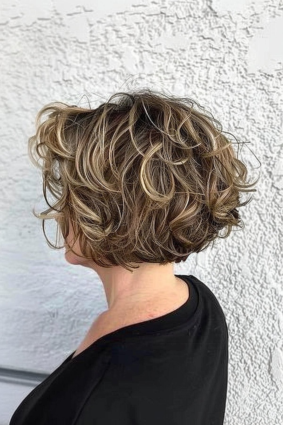 Woman with curly stacked bob and natural highlights